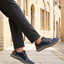 Lifestyle view of bugatti Compton dark blue comfort sneakers, with brown accent, worn with gray dress pants.
