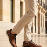 Bugatti Rickson cognac comfort sneakers, side view. Brown textured leather shoes with laces and side zipper, worn with tan pants.
