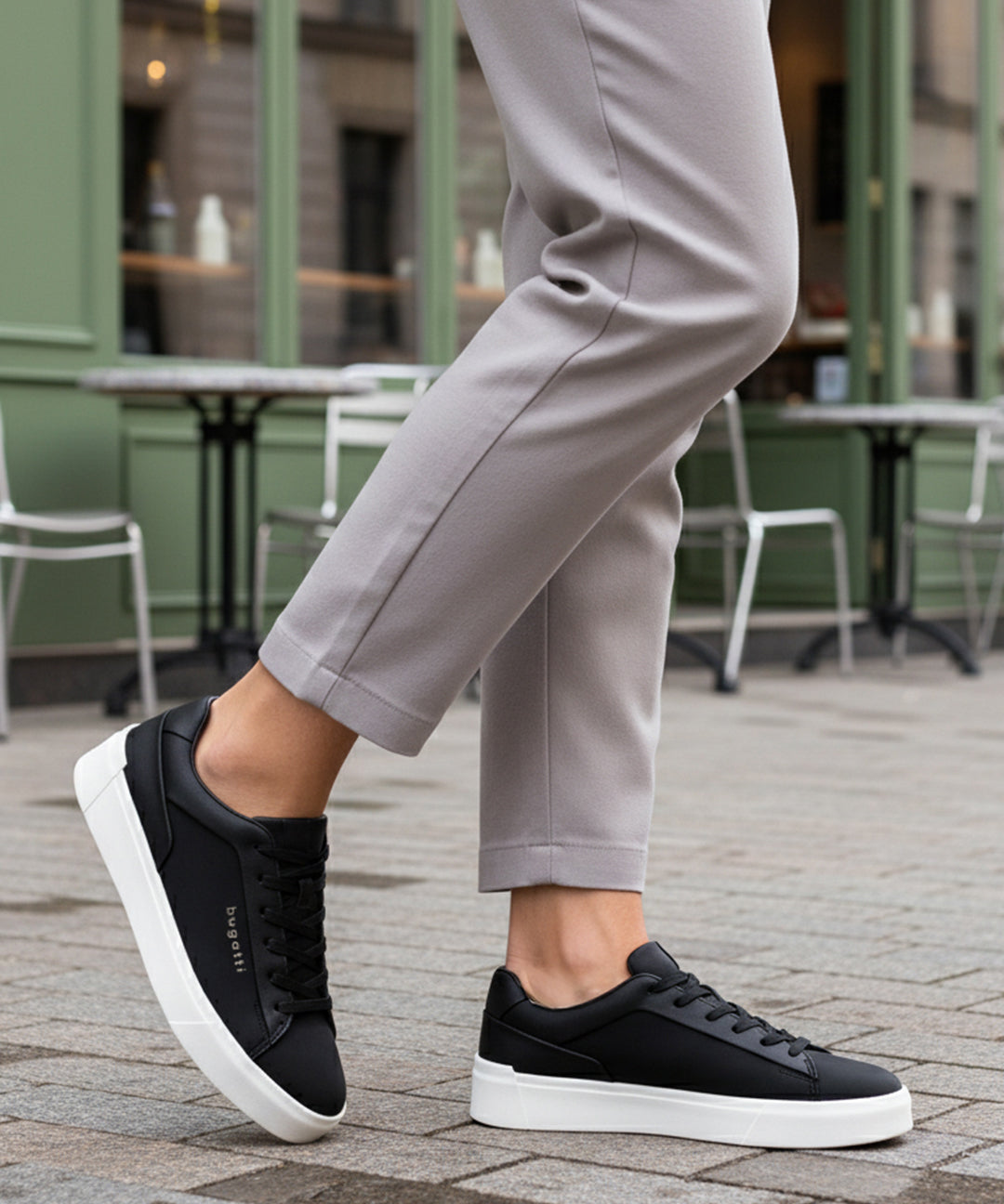 Lifestyle shot of bugatti Gunter black sneakers with a white sole, worn with grey pants.
