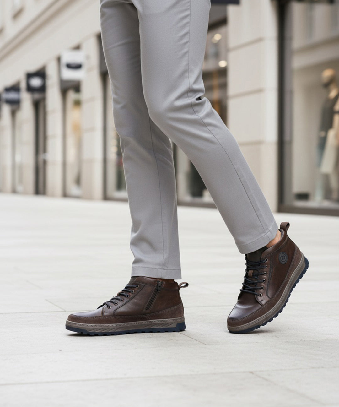 Lifestyle view of a man wearing Bugatti Exeter high-top sneakers in dark grey leather with laces, paired with grey pants.