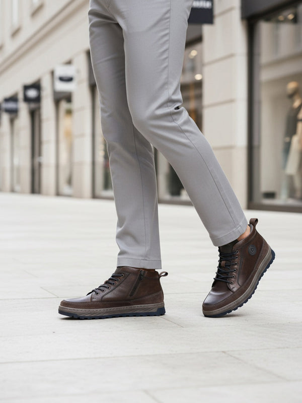 Lifestyle view of a man wearing Bugatti Exeter high-top sneakers in dark grey leather with laces, paired with grey pants.