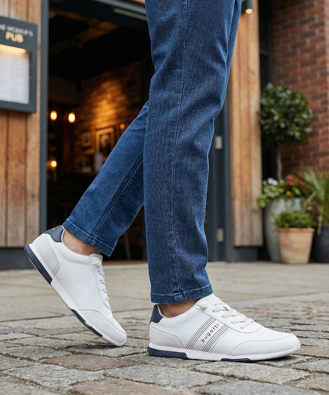 Lifestyle shot of white Bugatti sneakers with striped detail worn with blue jeans.