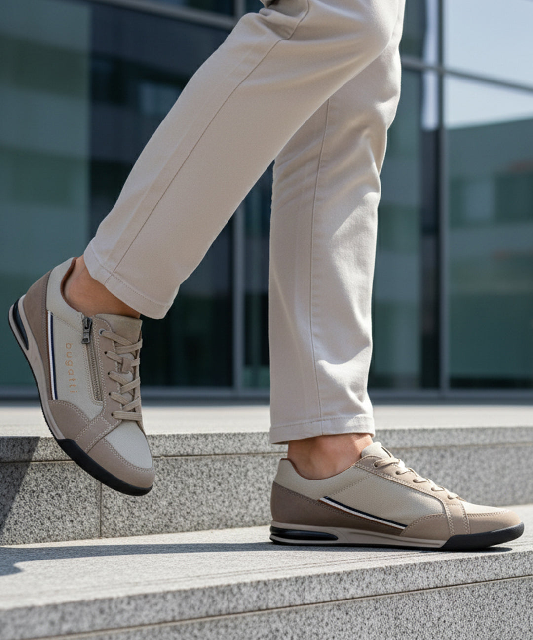 Lifestyle shot of bugatti Trevor beige comfort sneakers, with a zipper, worn with beige pants on steps.
