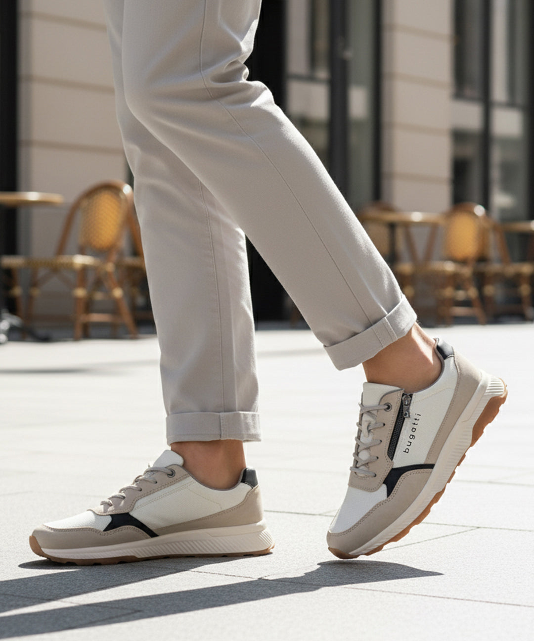 Lifestyle shot of bugatti Jerit Beige Comfort Sneakers, with zipper detail, worn with cuffed grey pants on a paved surface.
