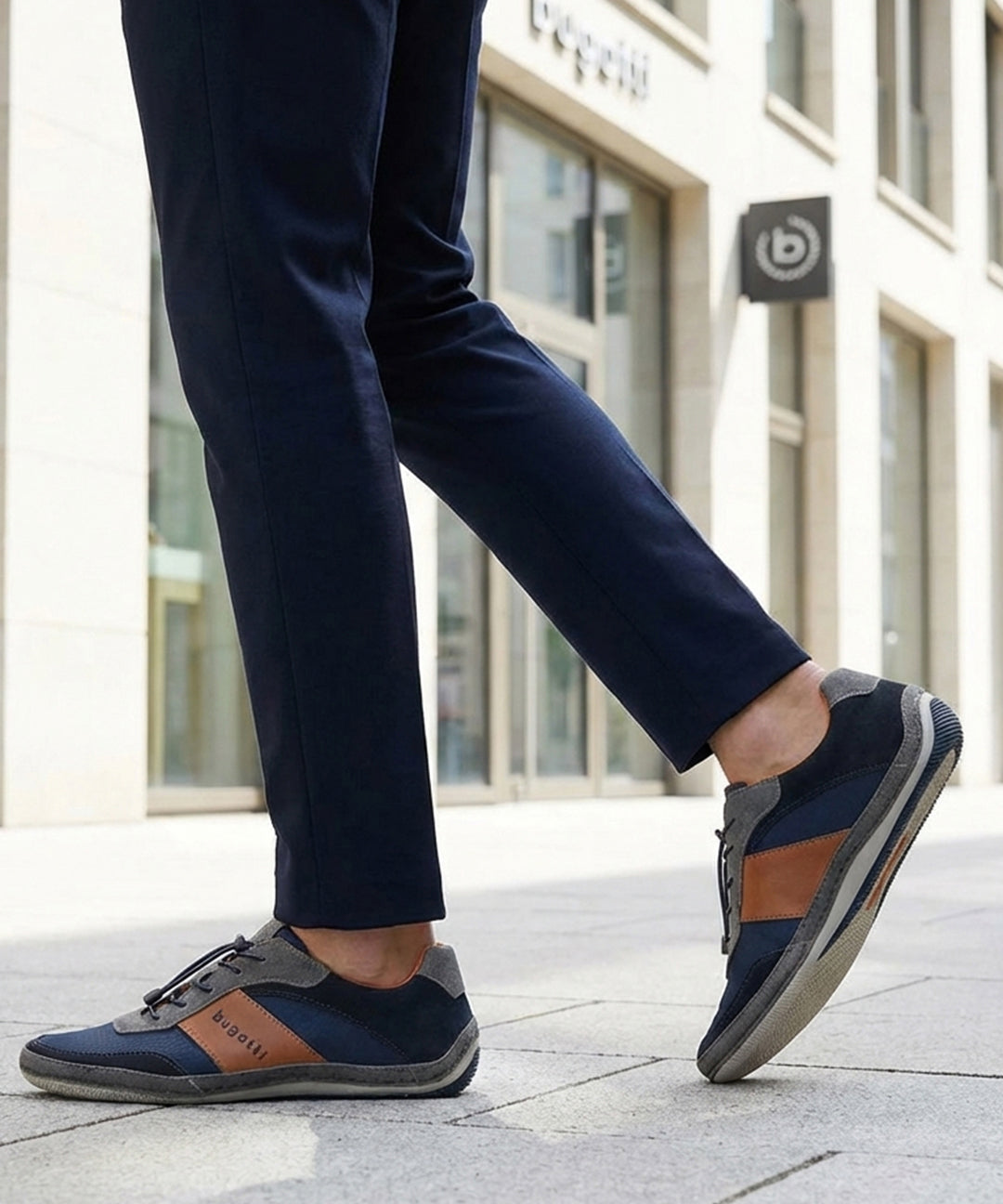 Lifestyle shot of a person wearing navy trousers and bugatti Canario Grey sneakers with brown leather accents.