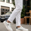 Lifestyle shot of bugatti Humus white premium leather mid-top sneakers with dark blue heel detail, worn with white pants.
