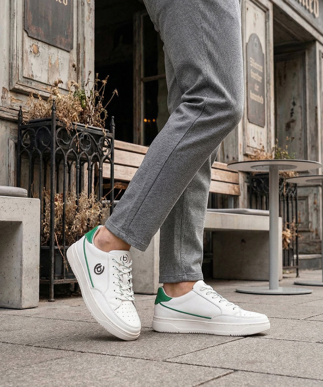 Lifestyle shot of white bugatti Humus Premium Leather Comfort Mid Top Sneakers with green accents, worn with gray pants.