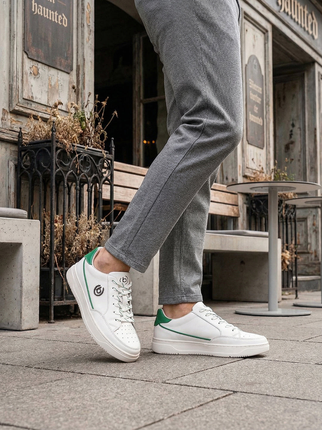 Lifestyle shot of white bugatti Humus Premium Leather Comfort Mid Top Sneakers with green accents, worn with gray pants.