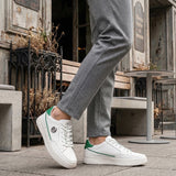Lifestyle shot of white bugatti Humus Premium Leather Comfort Mid Top Sneakers with green accents, worn with gray pants.