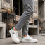 Lifestyle shot of white bugatti Humus Premium Leather Comfort Mid Top Sneakers with green accents, worn with gray pants.