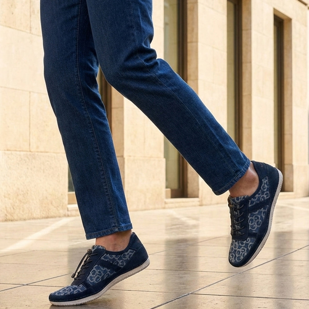 Lifestyle shot of bugatti Bimini light blue comfort sneakers with a floral pattern, paired with denim jeans.
