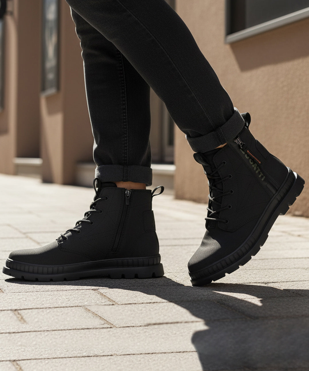 Lifestyle shot of bugatti Pallario comfort black casual boots, with zipper detail and lug sole, worn with dark rolled jeans.
