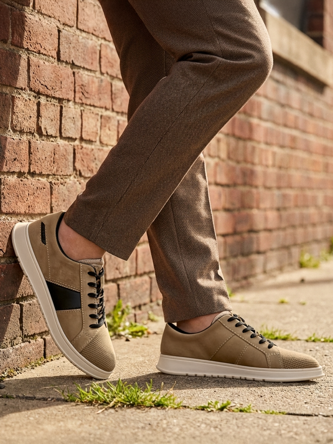 bugatti Fiero beige leather sneakers with black laces and a white sole, worn with brown trousers.
