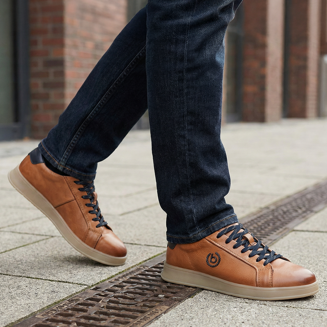 Lifestyle close-up of bugatti Fiero cognac leather sneakers with dark denim jeans on a city street.