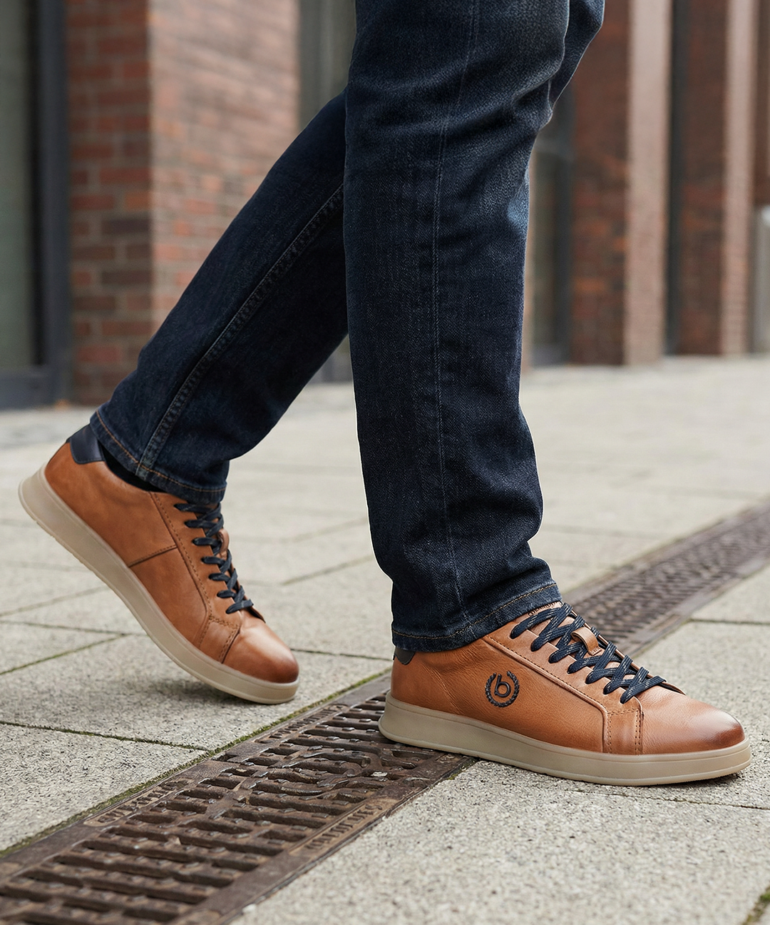 Lifestyle close-up of bugatti Fiero cognac leather sneakers with dark denim jeans on a city street.