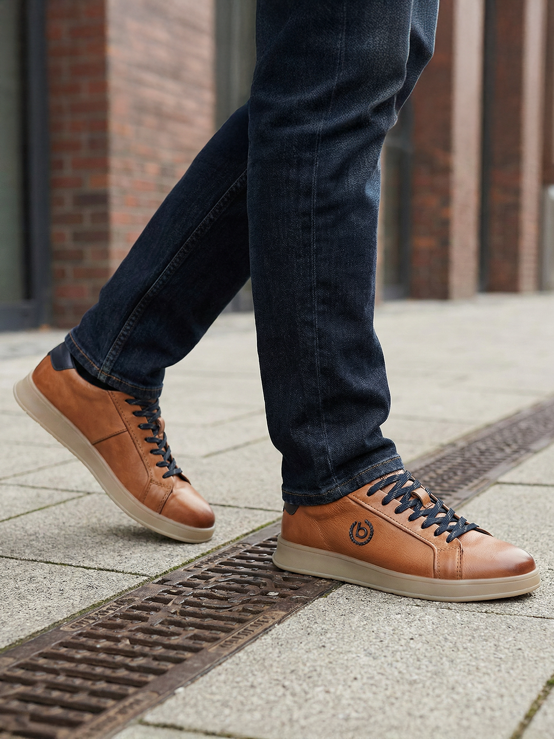 Lifestyle close-up of bugatti Fiero cognac leather sneakers with dark denim jeans on a city street.