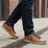 Lifestyle close-up of bugatti Fiero cognac leather sneakers with dark denim jeans on a city street.
