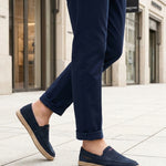 Lifestyle image of bugatti Spendril dark blue leather slip-on shoes with a jute sole, worn with cuffed navy pants.
