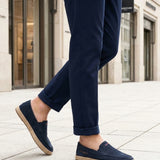 Lifestyle image of bugatti Spendril dark blue leather slip-on shoes with a jute sole, worn with cuffed navy pants.
