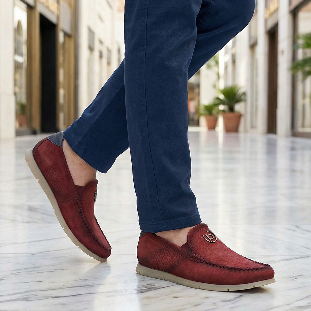 Lifestyle shot of bugatti Clipperton red leather slip-on casual shoes with blue pants, worn on marble floor.