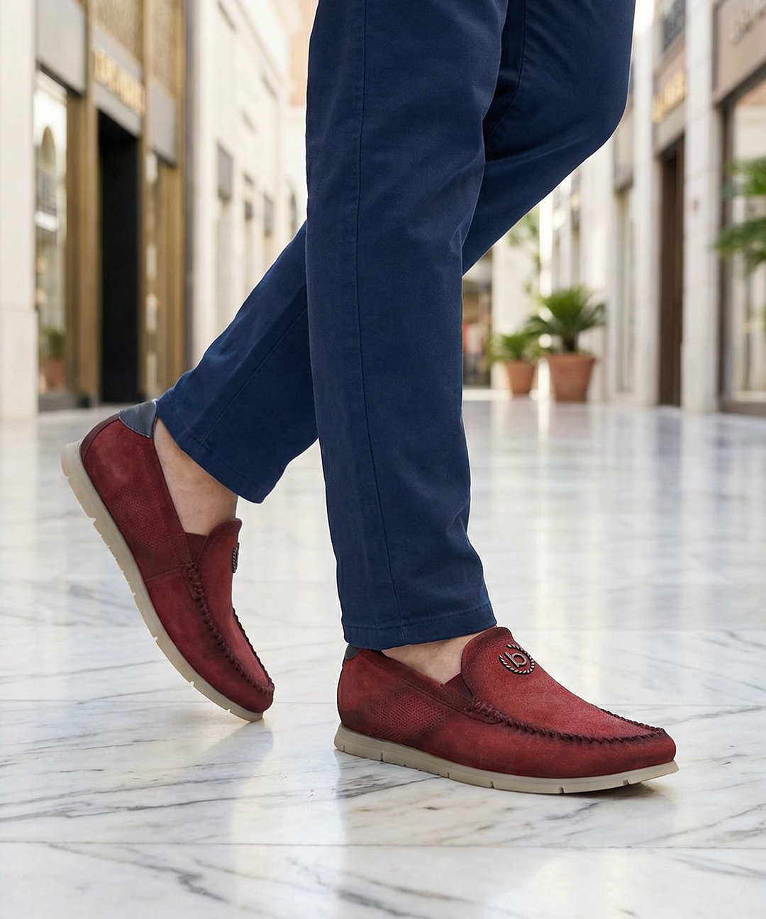 Lifestyle shot of bugatti Clipperton red leather slip-on casual shoes with blue pants, worn on marble floor.