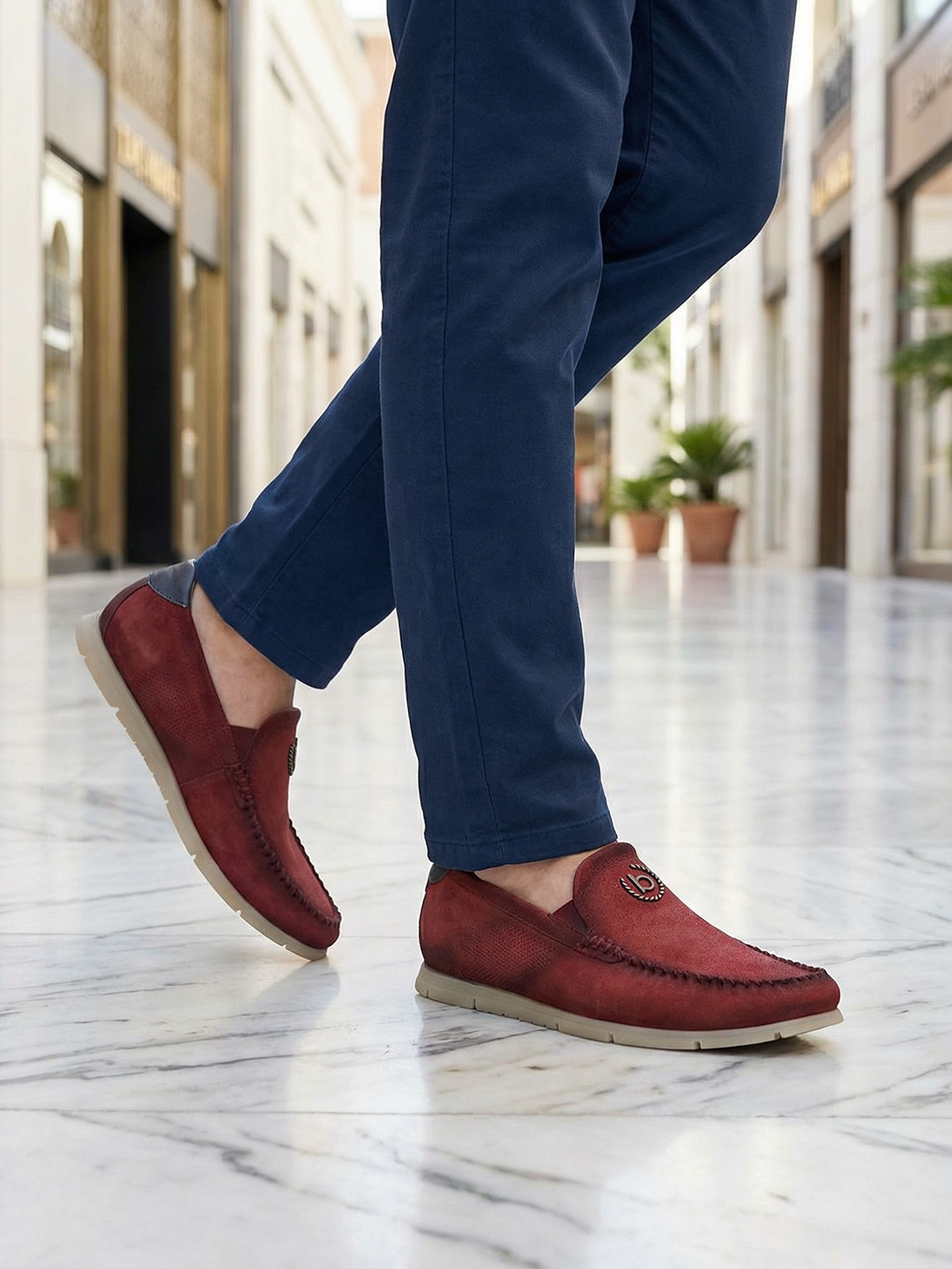 Lifestyle shot of bugatti Clipperton red leather slip-on casual shoes with blue pants, worn on marble floor.