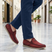 Lifestyle shot of bugatti Clipperton red leather slip-on casual shoes with blue pants, worn on marble floor.