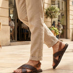Lifestyle view of bugatti Cobie dark brown leather sandals with adjustable back strap, paired with beige linen pants.