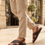 Lifestyle view of bugatti Cobie dark brown leather sandals with adjustable back strap, paired with beige linen pants.