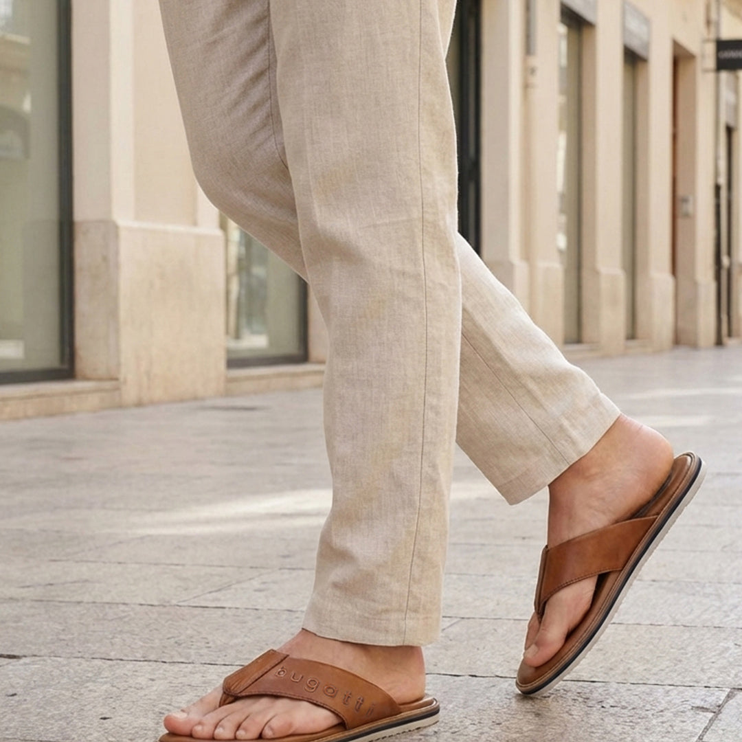 Lifestyle image of bugatti Cobie cognac leather thong sandals worn with casual tan pants in a city setting.