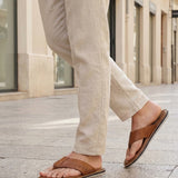 Lifestyle image of bugatti Cobie cognac leather thong sandals worn with casual tan pants in a city setting.