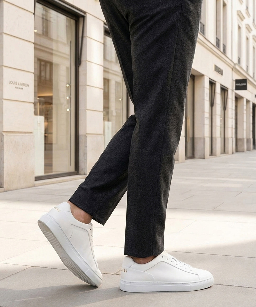 Lifestyle shot of bugatti Fogg white premium leather sneakers, paired with grey trousers and white pavement.
