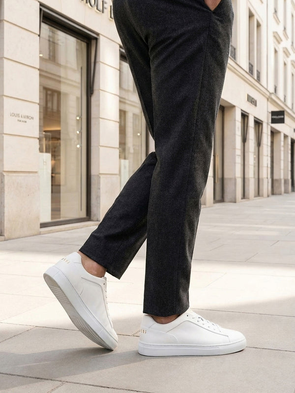 Lifestyle shot of bugatti Fogg white premium leather sneakers, paired with grey trousers and white pavement.
