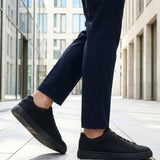 Lifestyle cropped shot of bugatti Fogg Black leather sneakers paired with dark trousers on tiled pavement.