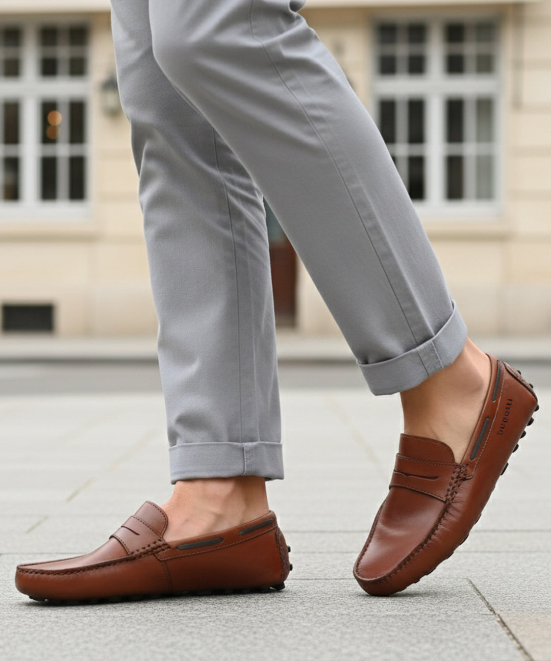 Lifestyle view of bugatti Manfield cognac leather slip-on shoes with penny loafer detailing and gray pants.