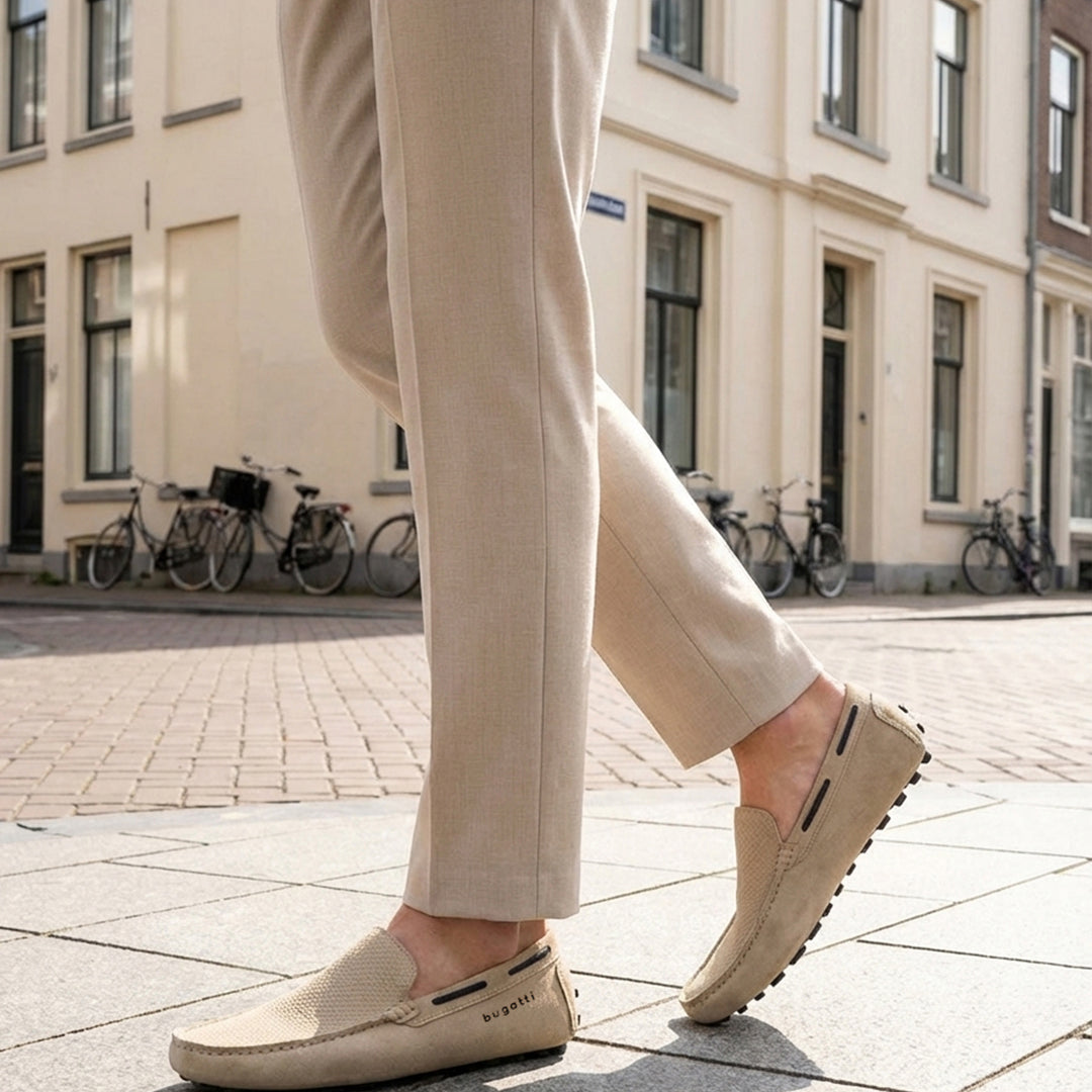 Lifestyle shot of bugatti Manfield sand-colored slip-on shoes in premium leather, worn with tan trousers on a city street.