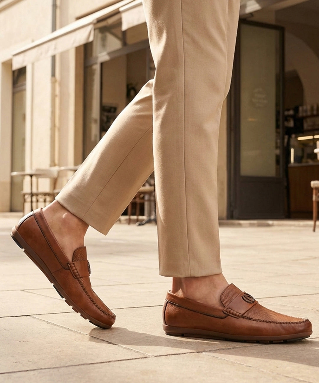 Lifestyle shot of bugatti cognac leather slip-on shoes with perforated details, paired with beige dress pants.
