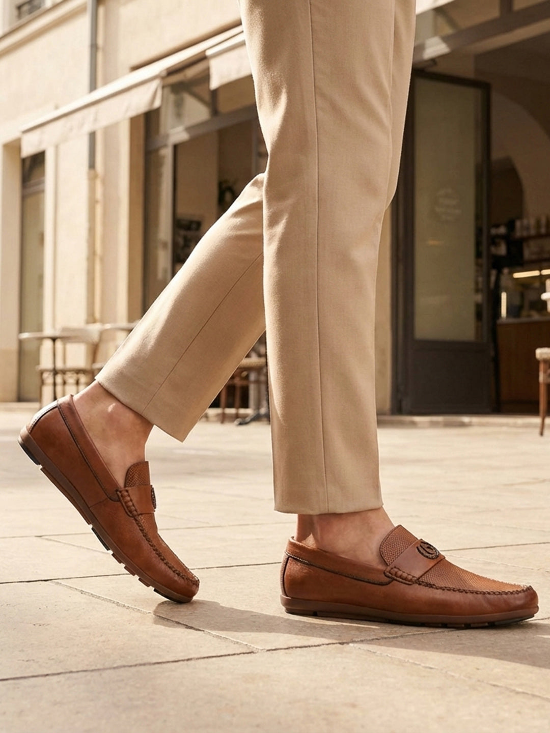 Lifestyle shot of bugatti cognac leather slip-on shoes with perforated details, paired with beige dress pants.
