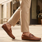 Lifestyle shot of bugatti cognac leather slip-on shoes with perforated details, paired with beige dress pants.
