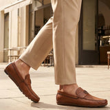 Lifestyle shot of bugatti cognac leather slip-on shoes with perforated details, paired with beige dress pants.

