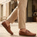 Lifestyle shot of bugatti cognac leather slip-on shoes with perforated details, paired with beige dress pants.
