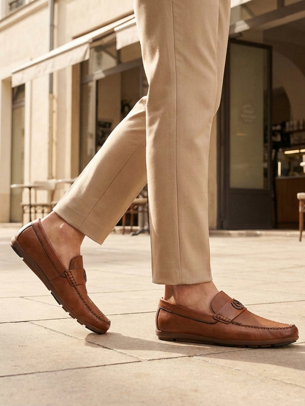 Lifestyle shot of bugatti cognac leather slip-on shoes with perforated details, paired with beige dress pants.
