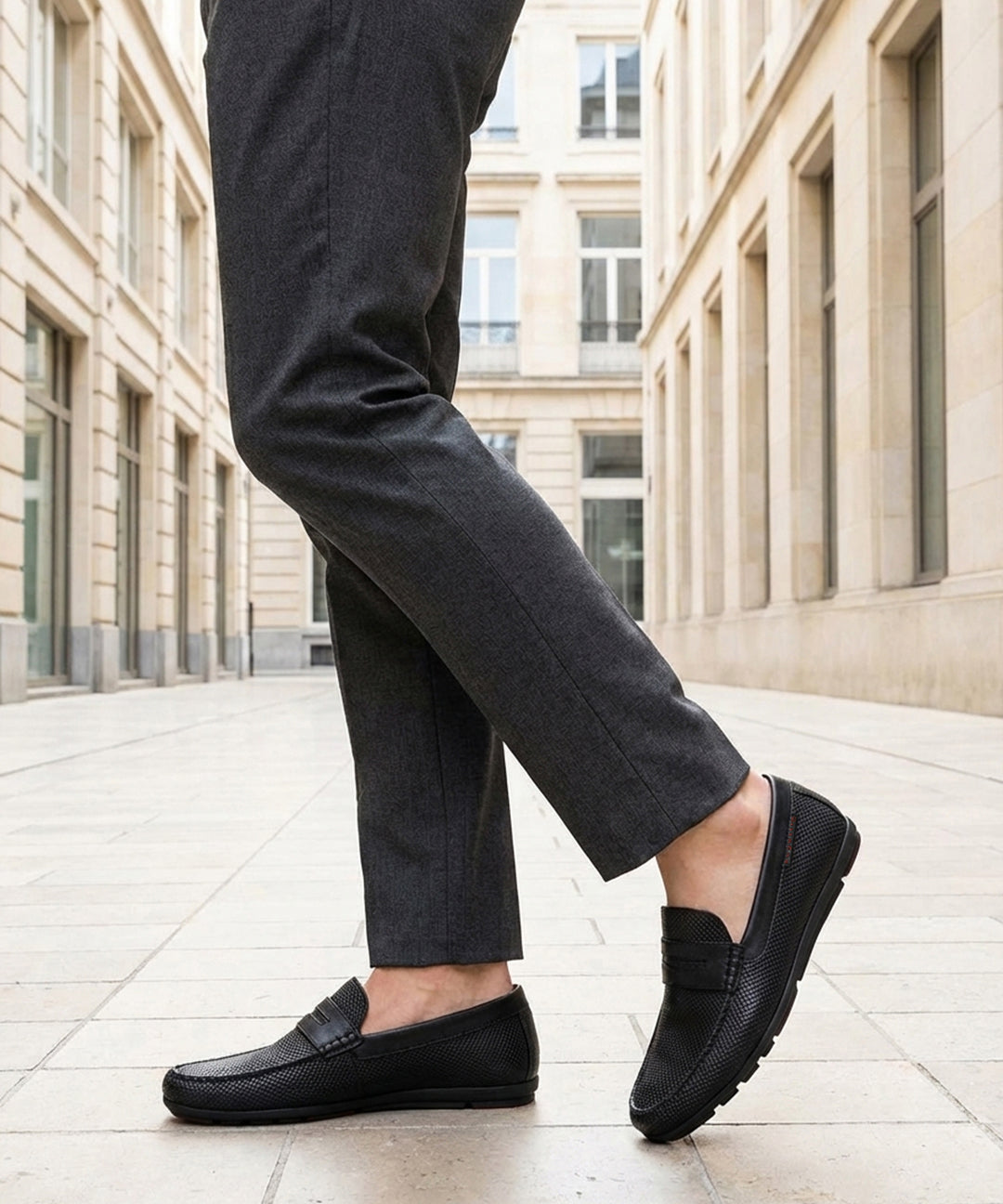bugatti Cobe black premium leather slip-on shoe, side view, paired with gray dress pants in a city setting.
