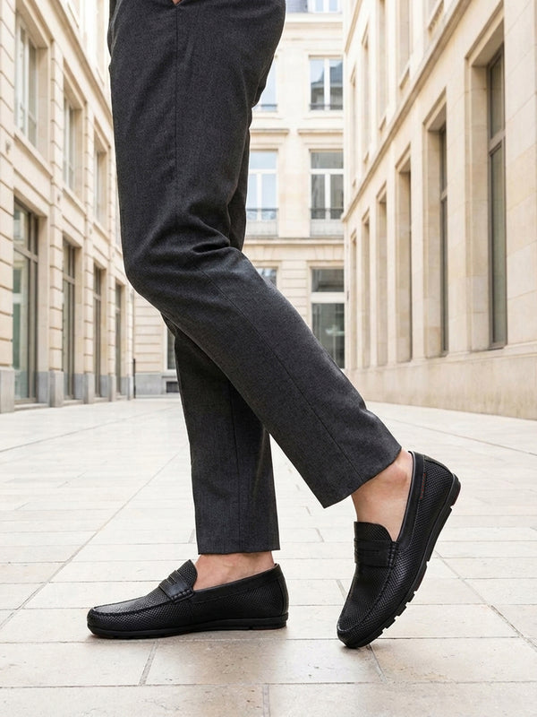 bugatti Cobe black premium leather slip-on shoe, side view, paired with gray dress pants in a city setting.
