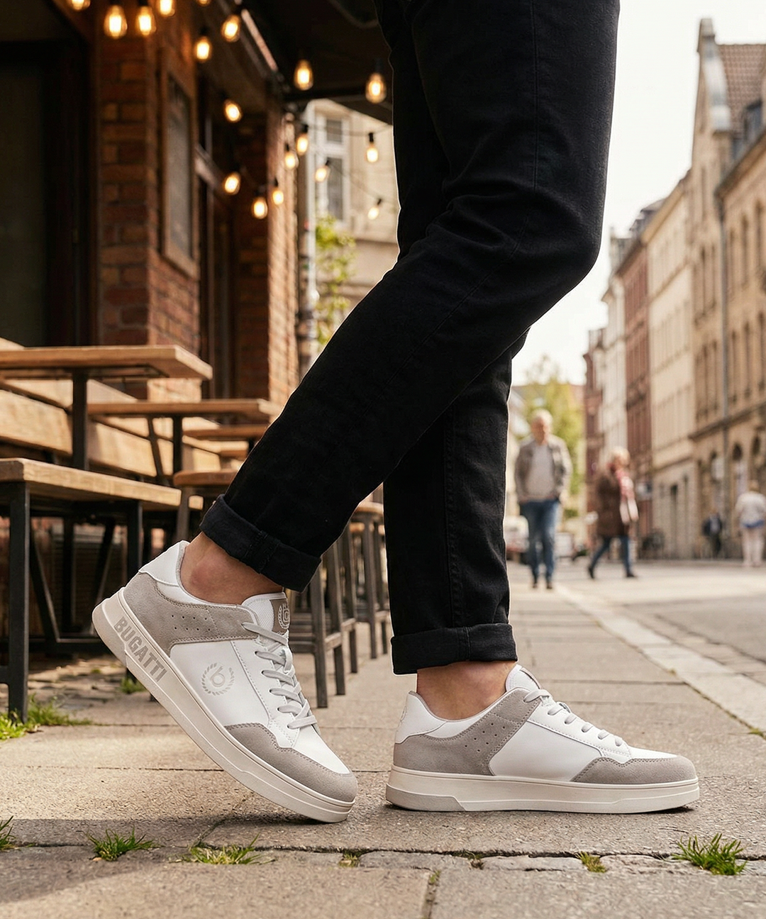 Lifestyle shot of bugatti Franc White sneakers in white leather and grey suede, worn with black jeans.