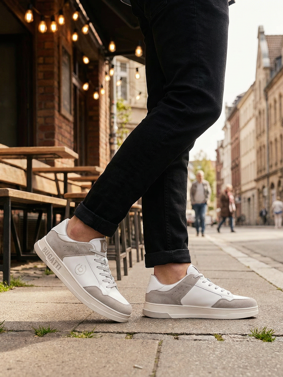 Lifestyle shot of bugatti Franc White sneakers in white leather and grey suede, worn with black jeans.
