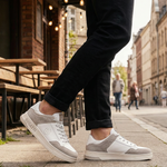 Lifestyle shot of bugatti Franc White sneakers in white leather and grey suede, worn with black jeans.