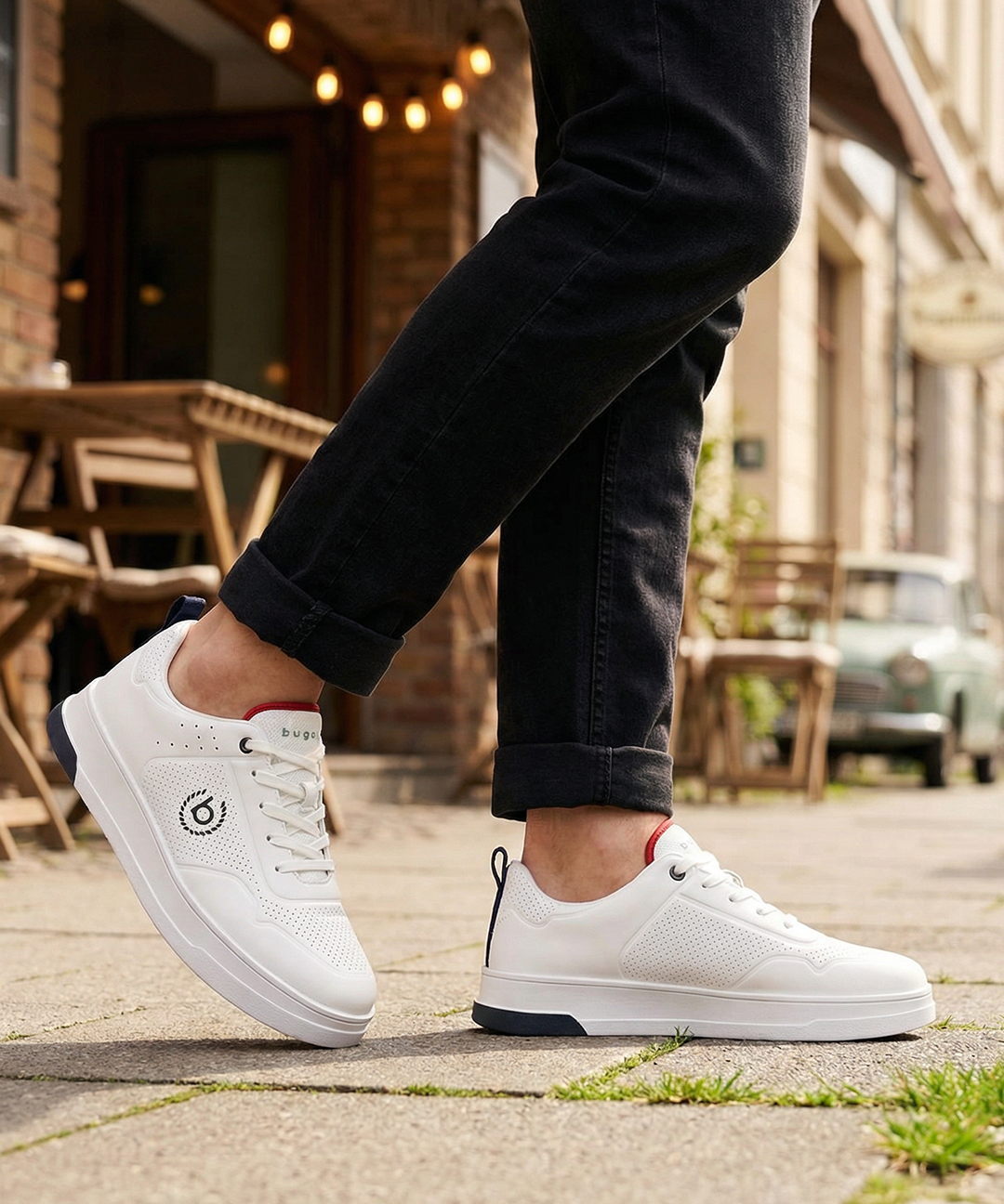 Lifestyle shot of bugatti Franc white leather sneakers, with perforated details, worn with dark jeans.
