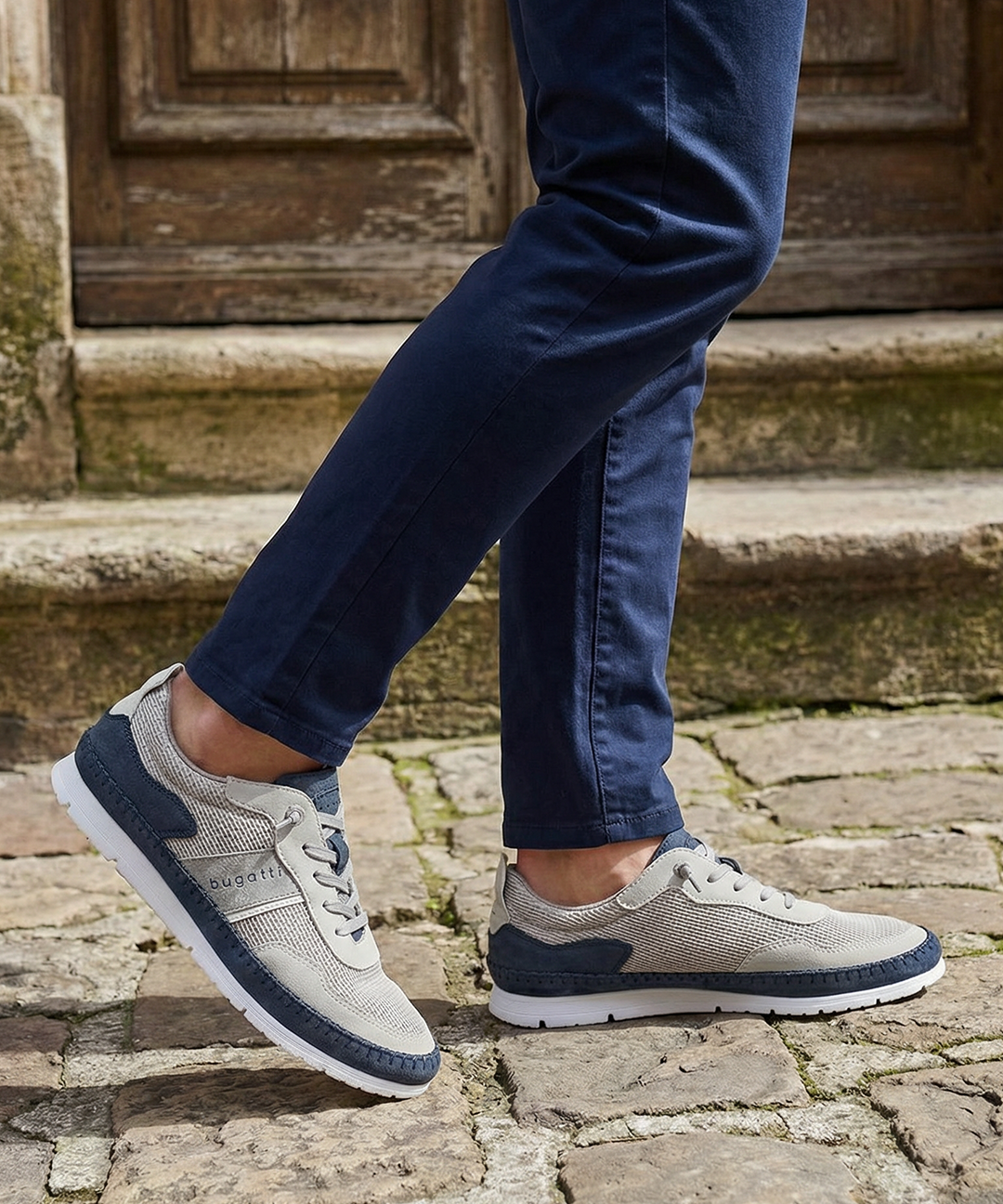 Lifestyle close-up of Bugatti Clipperton sand comfort low top sneakers with dark blue chinos on a stone surface.
