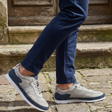 Lifestyle close-up of Bugatti Clipperton sand comfort low top sneakers with dark blue chinos on a stone surface.
